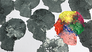 The photo shows several painted heads in gray with a brightly colored head in between 